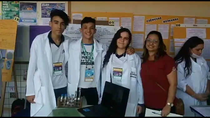 Abimael com colegas de jaleco e a orientadora durante uma apresentação de pesquisa