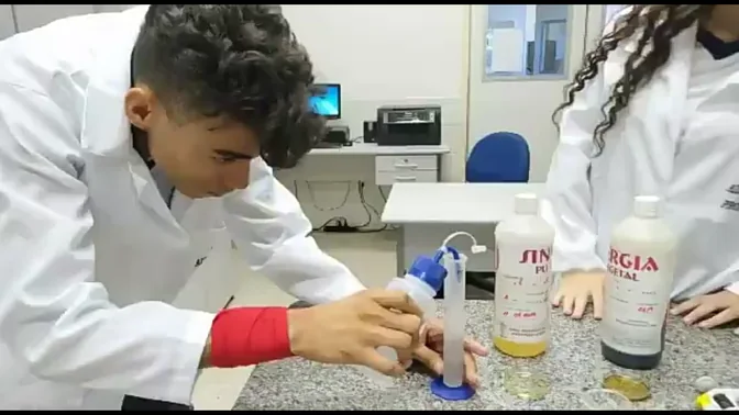 Abimael aos 17 anos, de jaleco, manuseando uma pipeta no laboratório